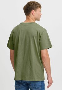 Camiseta de algodón verde oliva con corte relajado, mangas cortas y cuello redondo, con una textura suave y sin logotipos visibles.
