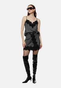 Abito grigio con pizzo nero, dalla silhouette aderente, spalline regolabili e cintura coordinata, abbinato a stivali alti lucidi neri.