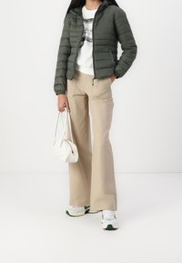 Oliwkowa kurtka puchowa z kapturem, biała bluzka z grafiką, beżowe szerokie spodnie i mała biała torebka. Teksturowany materiał i casualowy fason.