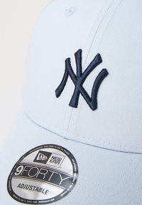 Boné de beisebol azul claro feito de tecido texturizado, apresentando um logotipo bordado dos New York Yankees em azul marinho e um autocolante circular preto da New Era.