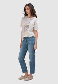 Lichtgrijs grafisch T-shirt met een ronde hals, voorzien van een kleurrijk gedrukt ontwerp; gecombineerd met middelblauwe spijkerbroek en lichtbeige mocassins.