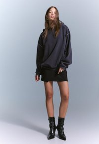 Hanorac oversized bleumarin cu detalii din ținte argintii, purtat cu o fustă mini neagră și cizme scurte negre lucioase. Material neted, croială lejeră.