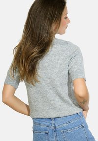 Pull en tricot gris clair à manches courtes avec un col rond et une texture subtile. Associé à un jean en denim bleu taille haute.