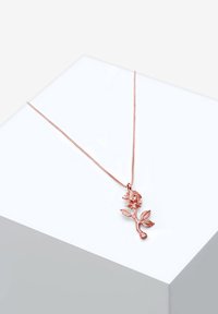 Roseformet vedhæng i rosaguld, fastgjort til en tynd kæde, med detaljerede kronblade og blade, præsenteret på en hvid pedestal.