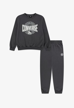 Completo felpa e pantaloni grigio carbone realizzato in tessuto morbido. La felpa presenta un grande logo bianco "Converse"; i pantaloni hanno polsini elasticizzati.