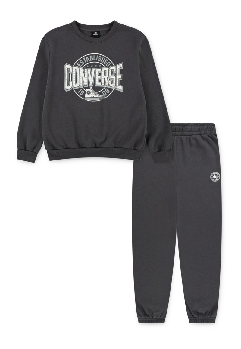 Koksrēļa pelēks sporta krekls un bikses, izgatavotas no mīkstas auduma. Sporta krekls ar lielu baltu "Converse" logo; biksēm ir elastīgas piedurknes.