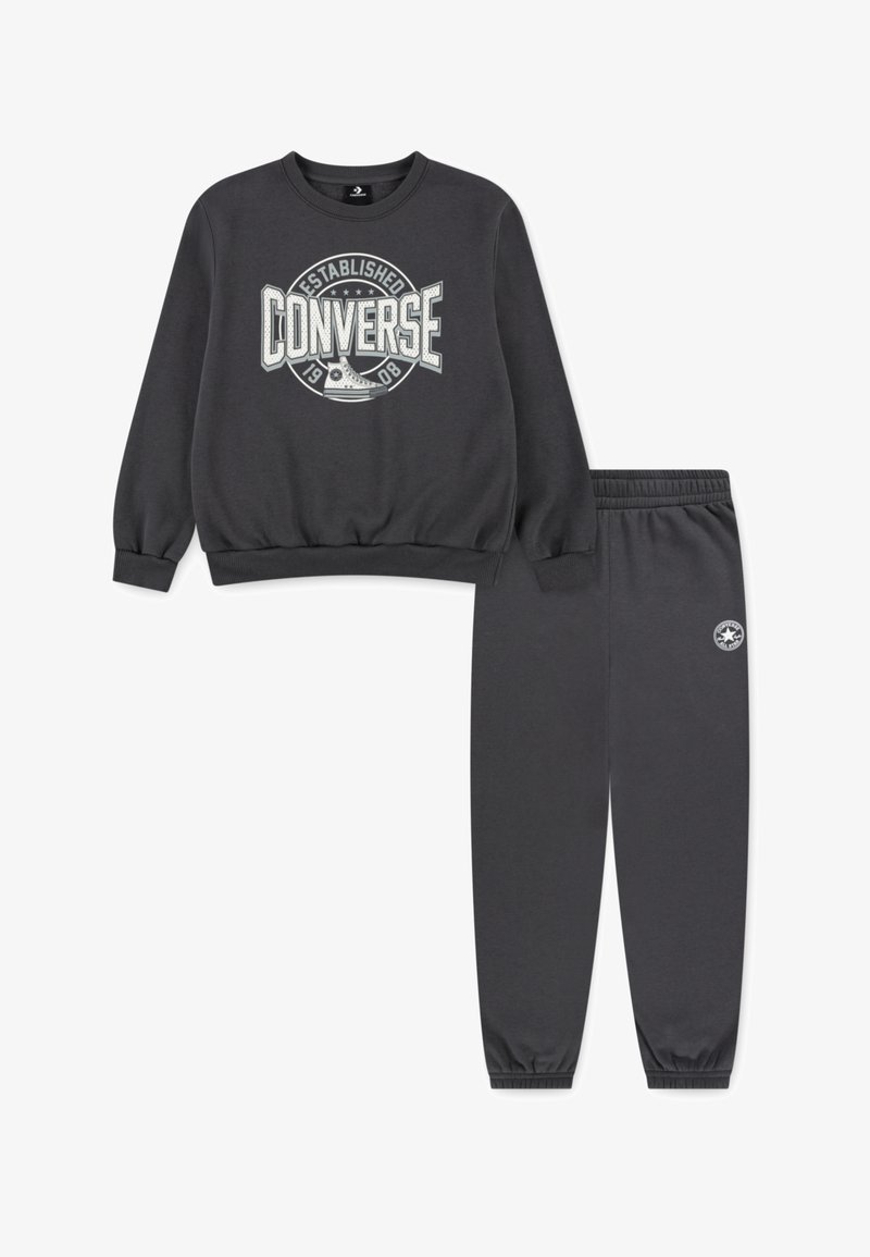 Párna szürke pulóver és nadrág szett, puha anyagból. A pulóveren nagy fehér "Converse" logó található; a nadrág rugalmas mandzsettával rendelkezik.