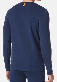 Granatowa koszula z długim rękawem i okrągłym dekoltem, wykonana z miękkiego materiału; na plecach znajduje się pomarańczowa metka, która dodaje koloru.