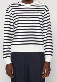 Felpa a righe in cotone bianco e nero; presenta bottoni sulle spalle, polsini a coste e un logo ricamato sul petto.