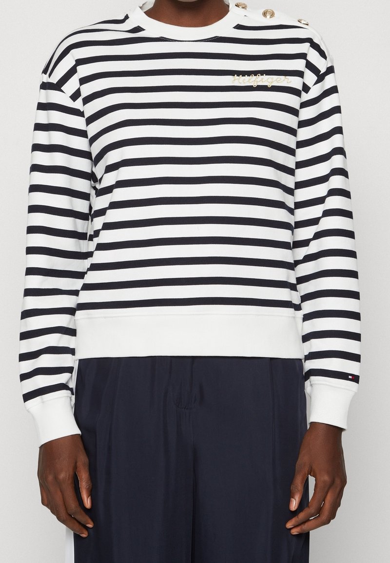 Felpa a righe in cotone bianco e nero; presenta bottoni sulle spalle, polsini a coste e un logo ricamato sul petto.