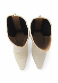 Botines de punta en ante crema con una textura suave. Forro interior de tela color tostado, con cremallera lateral para facilitar el calce.