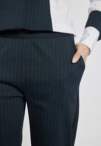 Niebieskie spodnie w paski morskie z cienkimi niebieskimi lamówkami, w luźnym kroju, z kieszeniami bocznymi, wykonane z gładkiego, teksturowanego materiału.