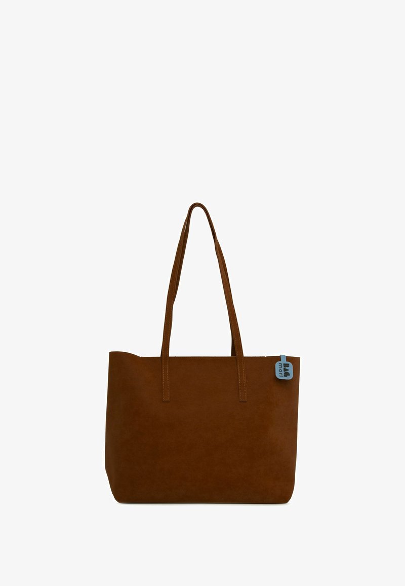 Braune Wildleder-Tote mit zwei langen Griffen, flacher Form, genähtem Rand und einem blauen Etikett, das die obere rechte Ecke akzentuiert.