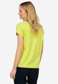 Camiseta de manga corta verde lima hecha de algodón suave, con mangas enrolladas y un corte relajado, combinada con pantalones oscuros.