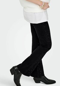 Svarte vide jeans med teksturert stoff, prydet med spredte sølvnitter langs siden. Kombinert med svarte ankelstøvler.