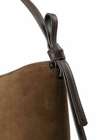 Borsa in suede marrone con tracolla in pelle scura. Presenta un bordo cucito e un dettaglio a nodo in pelle vicino alla cerniera, con una texture liscia.