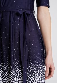 Námořnické šaty s tečkovaným vzorem, který na lemu přechází do bílé barvy, s opaskem na zavázání a krátkými rukávy. Měkká tkanina s hladkým povrchem.