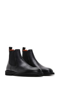 Coppia di stivali Chelsea in pelle nera con pannelli laterali elasticizzati e linguette, esposti su uno sfondo bianco.
