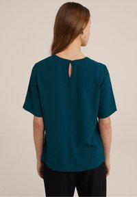 Tealfärgad kortärmad blus med en nyckelhålsglash och ett mjukt, texturerat tyg. Rakt snitt med en avslappnad passform.