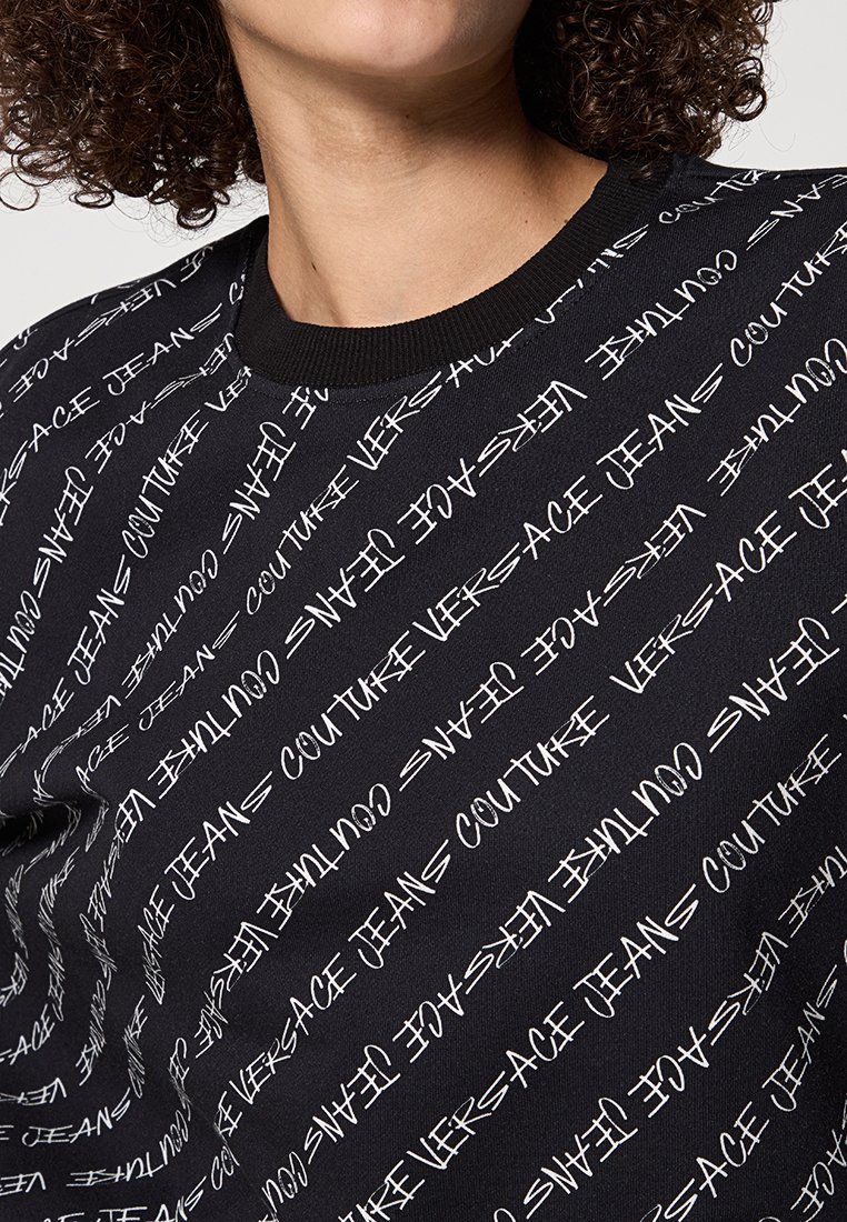 Sudadera negra con un patrón repetido de texto blanco que incluye "Versace Jeans Couture". Cuello acanalado y textura suave.