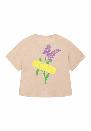 Beige oversized t-shirt met een ontwerp van paarse bloemen en een gele pleister op de achterkant, wat een speelse en artistieke stijl benadrukt.