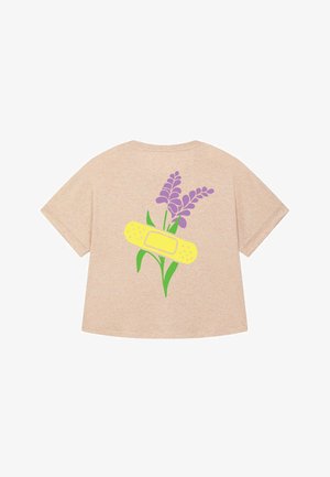 T-shirt oversize beige con un design di fiori viola e un cerotto giallo sul retro, che mette in evidenza uno stile giocoso e artistico.
