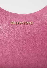 Pink textured leather surface with gold metal "VALENTINO" lettering centered near the top edge.
