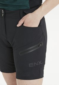 Svarta shorts med en sidoficka med dragkedja, förstärkt sömnad och varumärkeslogotypen "ENX" på det nedre benet. Slätt, lättviktigt tyg.