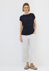 T-shirt bleu marine à manches courtes avec un design texturé sur le devant. Associé à un pantalon ample à rayures claires et des chaussures à enfiler beiges.