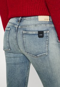 Jeans de mezclilla azul descoloridos con un ajuste ceñido. Las características incluyen dos bolsillos traseros y una etiqueta de marca en negro en el bolsillo derecho.