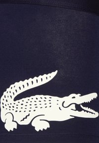 Tela azul marino con un logo de cocodrilo blanco destacado. El logo presenta escamas detalladas y un diseño de boca abierta.