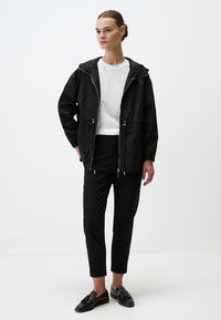 Zwarte hoodie met een rits aan de voorkant, elastische manchetten en een trekkoord in de taille. Draag het over een wit shirt en combineer het met zwarte broeken en instappers.