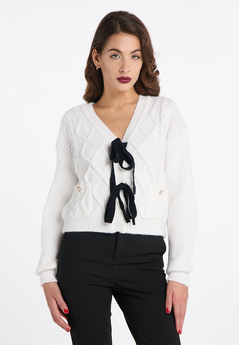 Weißer Strickcardigan mit Rautenmuster, V-Ausschnitt, schwarzen Bändern an der Vorderseite und zwei seitlichen Taschen mit Knöpfen.