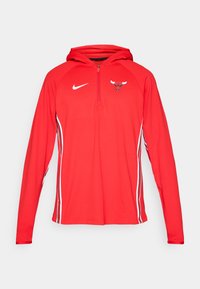 Rød Nike hettegenser med halv glidelås foran, med Bulls-logo på brystet og hvite sidekanter langs ermene. Glatt, lett stoff.
