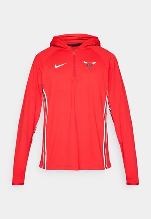 Piros Nike kapucnis pulóver fél cipzárral az elején, amelyen a mellkasán egy Bulls logó található és fehér oldalsávok futnak a ujjak mentén. Simább, könnyű anyag.