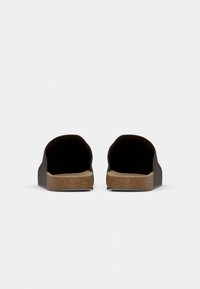 Črne natikače z širokimi odprtinami, gladkim zgornjim delom in svetlo rjavim teksturiranim podplatom. Ploska, pravokutna oblika z nizkim profilom.