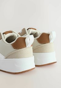 Baskets beige et marron avec une surface texturée, un design arrondi et une semelle en caoutchouc blanche. Présente une languette à l'arrière pour faciliter l'enfilage.