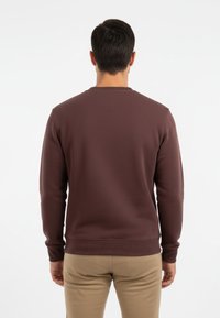 Sudadera de cuello redondo marrón hecha de una tela texturizada, con puños y dobladillo acanalados. Combinada con pantalones beige.