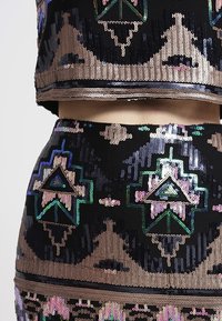 Černá souprava skládající se z krátkého topu a sukně, zdobená multicolorními flitry. Obsahuje geometrické vzory s kovovými akcenty a strukturované povrchy.