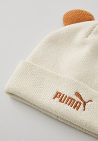 Cremfarbener Strickbeanie mit umgeschlagenem Bündchen, ausgestattet mit einem orangefarbenen aufgestickten "PUMA"-Logo und einem strukturierten braunen Pompon oben.