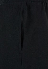 Gros plan sur une poche en tissu noir avec des coutures visibles et une ceinture élastique en haut.