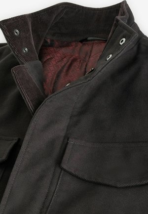 Veste en velours côtelé noir avec une doublure matelassée bordeaux. Équipée de boutons-pression et de poches avant doubles pour utilité et design.