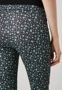 Les leggings floraux présentent un fond bleu marine foncé avec des motifs de fleurs claires vertes et blanches dispersés, fabriqués en un matériau doux et extensible.