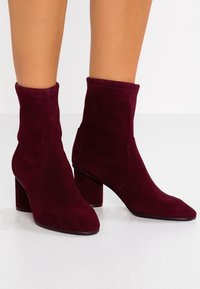 Botas cortas de ante burdeos con caña ajustada, punta puntiaguda y tacón grueso. Textura suave sin herrajes ni patrones visibles.