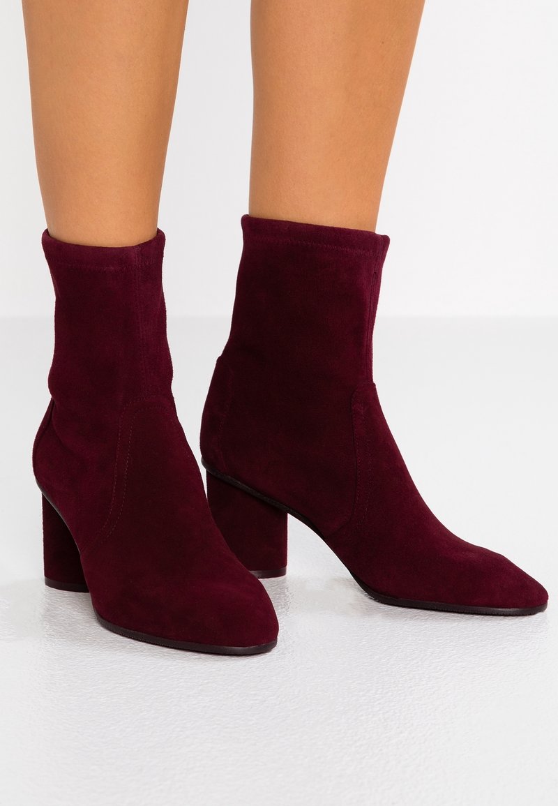 Botas cortas de ante burdeos con caña ajustada, punta puntiaguda y tacón grueso. Textura suave sin herrajes ni patrones visibles.