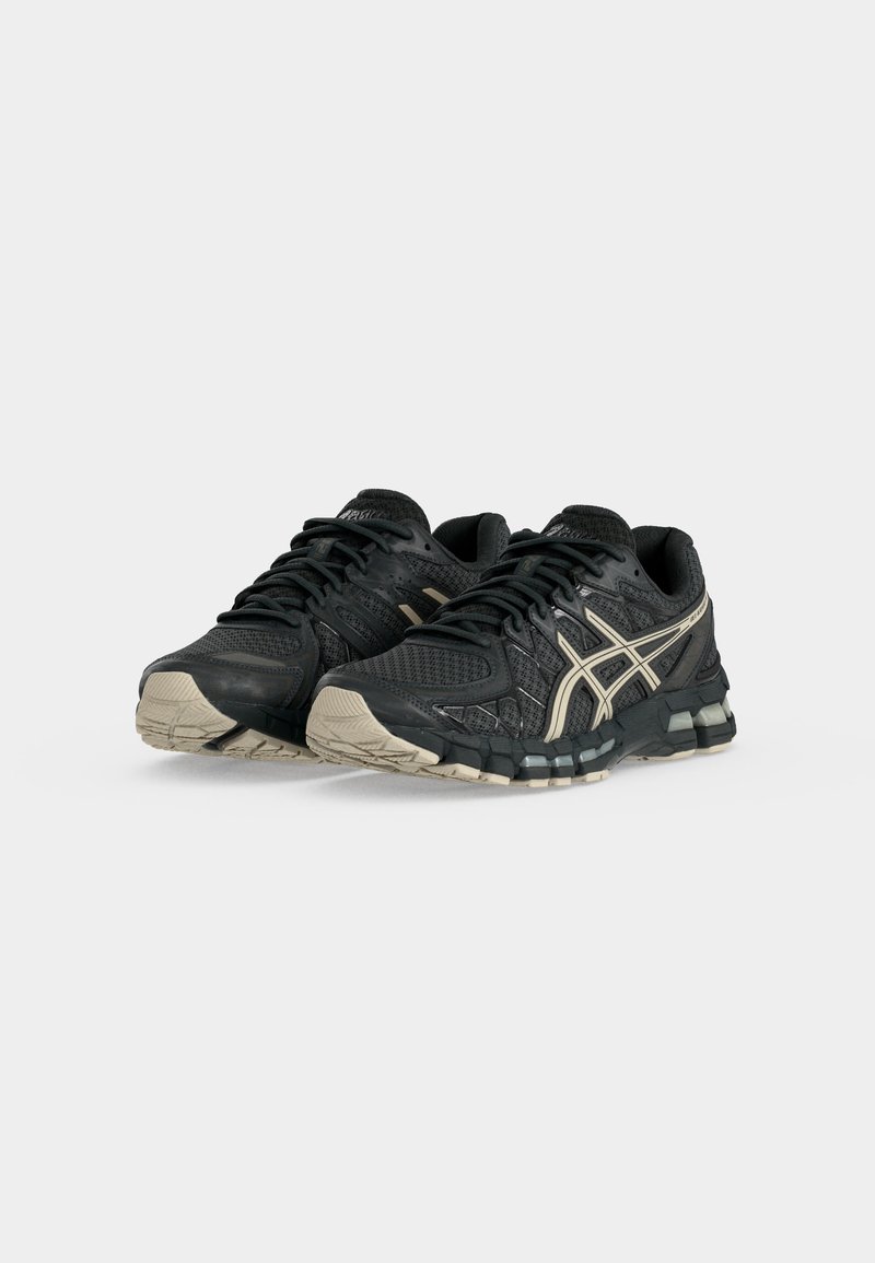 Par de zapatillas ASICS negras y beige para correr con parte superior de malla y material sintético, suela acolchada y cierre de cordones sobre fondo blanco.