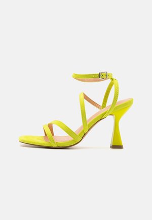 Sandale à talons hauts en daim jaune avec un design à plusieurs brides, bride de cheville réglable et un talon épais jaune avec une accentuation marron.