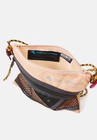 Pfirsichfarbene Nylontasche mit schwarzem Netzüberzug, Reißverschluss, buntem Kordelgriff und Innenetikett. Kompakte und funktionale Gestaltung.