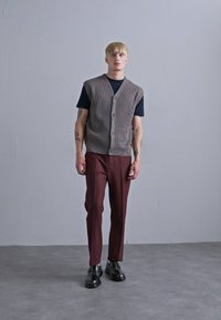 Hallikaelusega triibuline kootud vest musta T-särgi peal, koos burgundi värvi puhaste pükstega ja mustade nahkkingadega. Minimalistlik disain ja sobiv siluett.