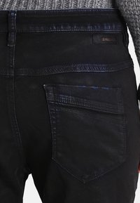 Černé džíny z denimu s hladkou strukturou, které mají zadní kapsu a nenápadné logo Diesel poblíž pasu.